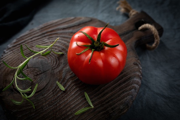 Reifer Bio-Tomaten-Rosmarin-Zweig auf einem alten Schneidebrett