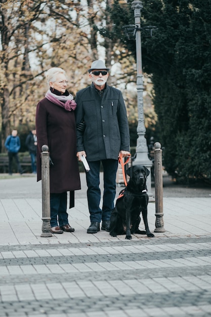 Reifer blinder Mann mit einem langen weißen Stock und seine Frau, die mit ihrem Blindenhund spazieren geht.