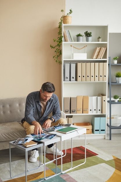 Reifer Fotograf, der auf dem Sofa sitzt und Fotos mit Landschaften betrachtet, wählt er seine beste Arbeit aus