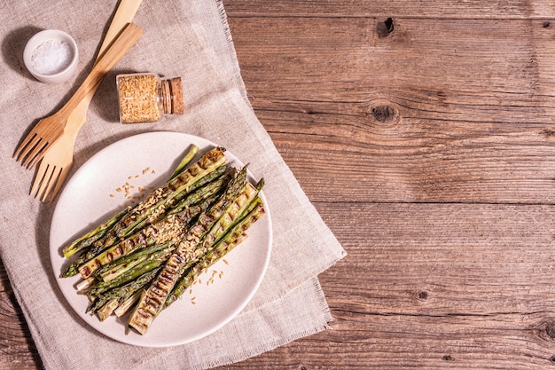 Reifer gegrillter Spargel. Holzbesteck, gesundes Lebensmittelkonzept. Trendiges hartes Licht, dunkler Schatten. Vintage Brettertisch, Draufsicht