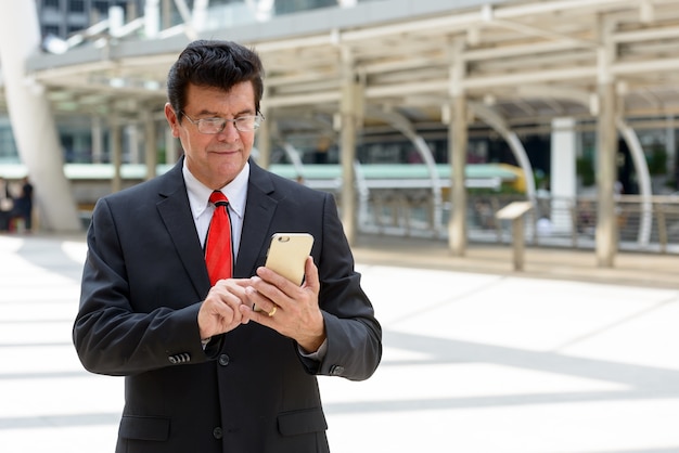 Reifer Geschäftsmann, der Handy vor dem modernen Gebäude an der Stadt Bangkok verwendet