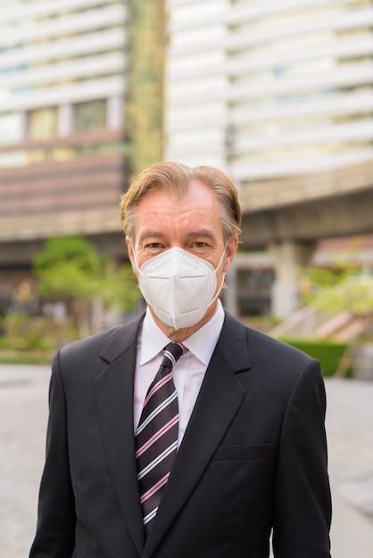 Reifer Geschäftsmann, der Maske zum Schutz vor Coronavirus-Ausbruch in der Stadt im Freien trägt