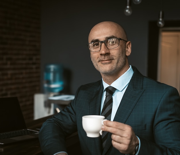 Reifer Geschäftsmann in einem Geschäftsanzug, der eine Tasse Kaffee in einer Cafeteria des Bürogebäudes hält