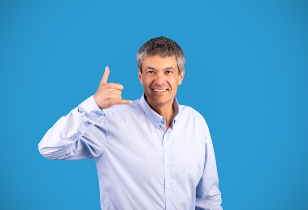 Reifer grauer Mann zeigt „Ruf mich an“-Geste auf blauem Hintergrund