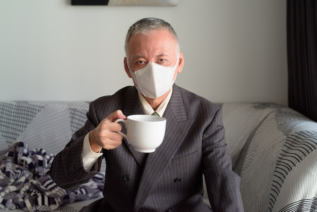 Reifer japanischer Geschäftsmann mit Maske, die zu Hause unter Quarantäne bleibt