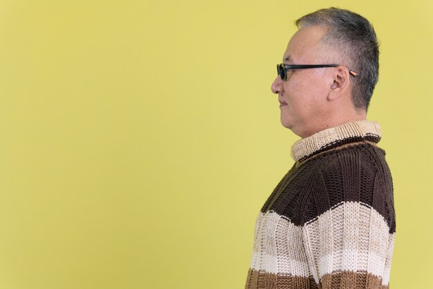 reifer japanischer Mann mit Rollkragenpullover bereit für Winter gegen Chroma Key mit grüner Wand
