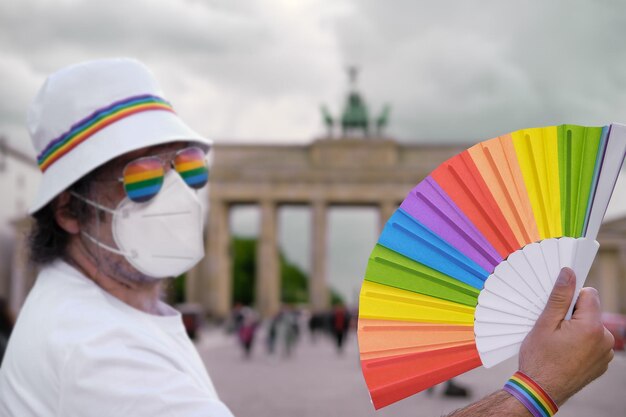 Reifer kaukasischer LGBT-Mann in Berlin mit Regenbogenfächer und Band auf weißem Sommerhut