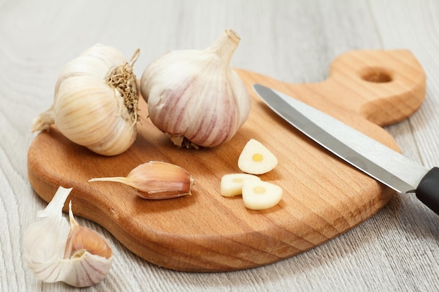 Reifer Knoblauch und Edelstahlmesser auf Holzschneidebrett mit grauem Hintergrund