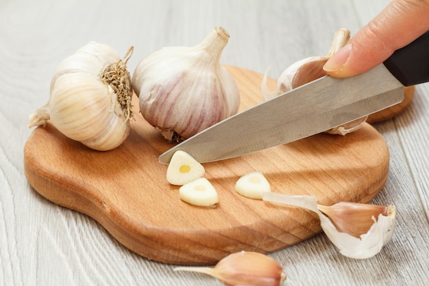 Reifer Knoblauch und eine Hand mit einem Edelstahlmesser auf einem Holzschneidebrett