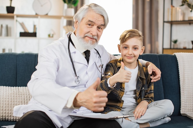 Reifer Mann Arzt im weißen Kittel und Stethoskop auf den Schultern im Gespräch mit kranken Jungen Patienten