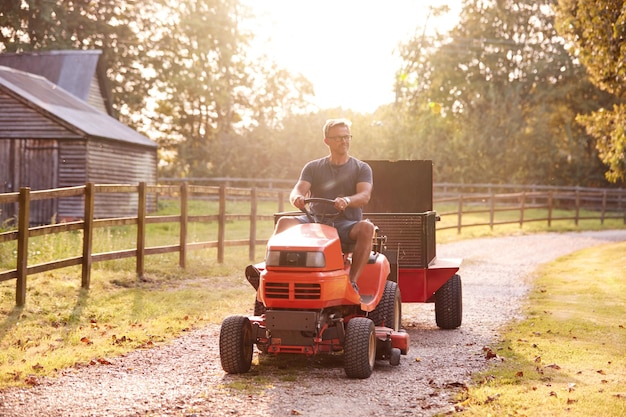 Reifer Mann, der auf dem Rasenmäher auf dem Gartenweg fährt