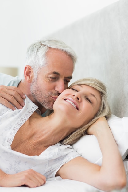 Reifer Mann, der die Backe der Frau im Bett küsst