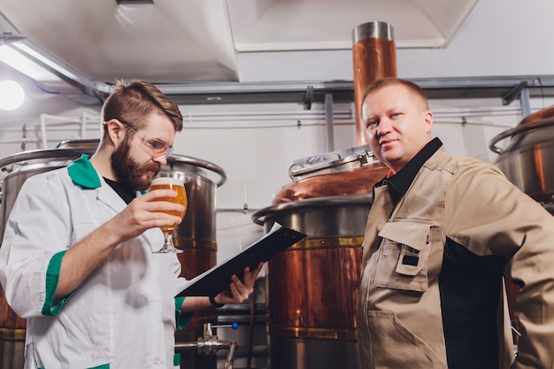 Foto reifer mann, der die qualität des handwerksbiers an der brauerei überprüft. inspektor, der an der alkoholherstellungsfabrik überprüft bier arbeitet. mann in der brennerei qualitätskontrolle des fassbiers überprüfend.