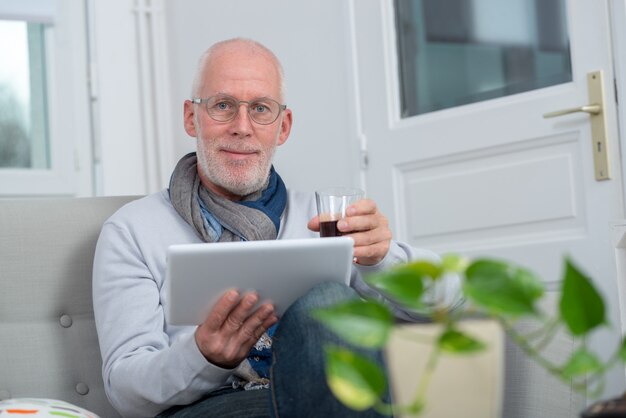 Reifer Mann, der digitale Tablette auf Sofa im Wohnzimmer verwendet