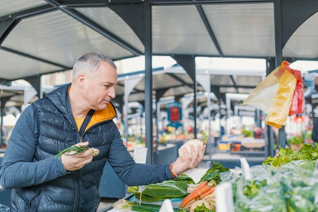 Reifer Mann, der Gemüse am Markt der Landwirte auswählt.