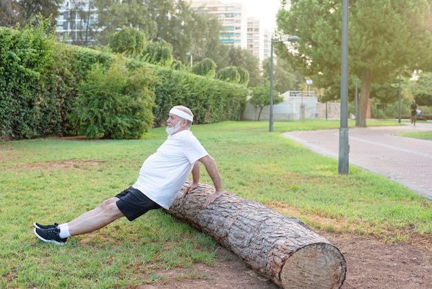 Reifer Mann, der im Park Dips-Übungen für Trizeps- und Bizepsmuskel übt Seitenansicht eines älteren Mannes, der mit einem Baumstamm trainiert