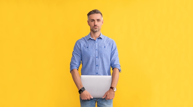 Reifer Mann, der Laptop auf gelbem Hintergrund hält Geschäftsmann