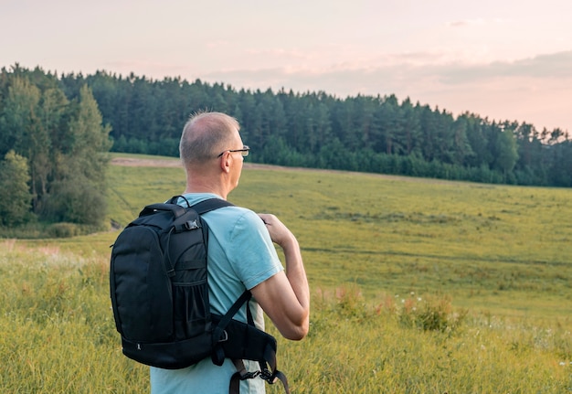 Reifer Mann, der mit Rucksack wandert, der im Feld wandert und das Sky-Solo-Reisekonzept genießt