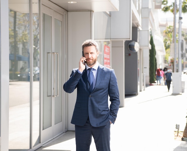 Reifer mann geschäftsmann im sachlichen anzug spricht am telefon außerhalb der bürokommunikation