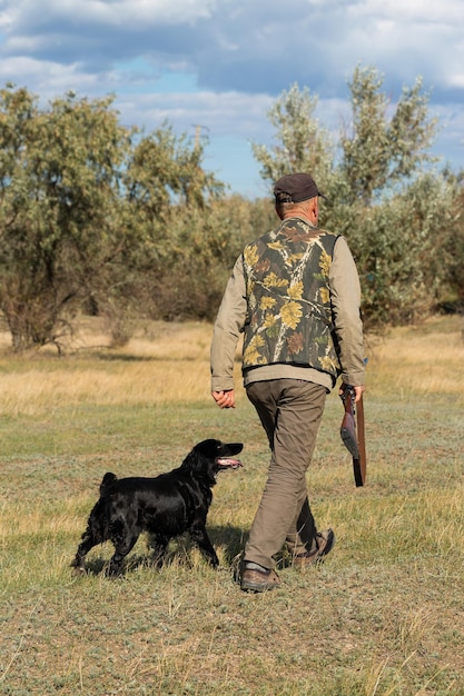 Reifer Mann Jäger mit Waffe beim Gehen auf dem Feld mit Ihren Hunden