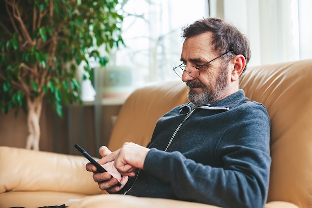 Reifer Mann mit Brille SMS oder Messaging oder Suchen oder Lesen auf einem modernen Smartphone Senioren mit Technologiekonzept