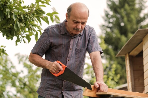 Reifer Mann mit Schnurrbart, der eine Säge in der Hand hält Sägen von Brennholz ernten