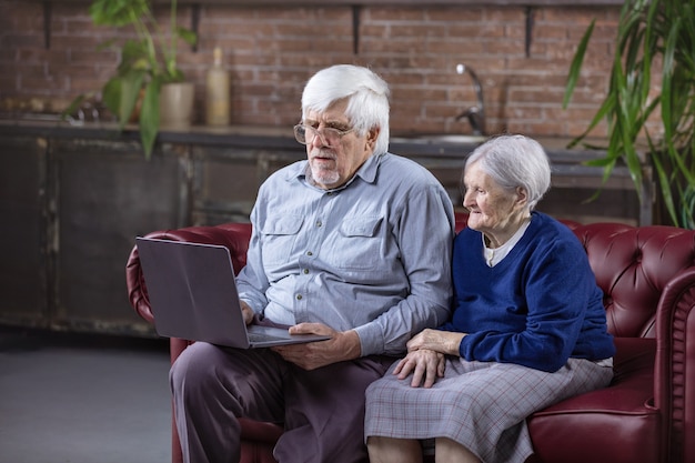 Foto reifer mann und ältere frau, die laptop beim sitzen auf der couch verwenden. video ansehen oder im internet auf dem laptop surfen.