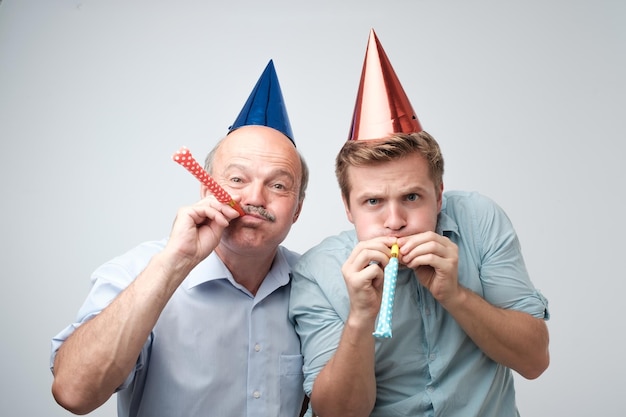 Reifer Mann und sein kleiner Sohn feiern alles Gute zum Geburtstag mit lustigen Mützen