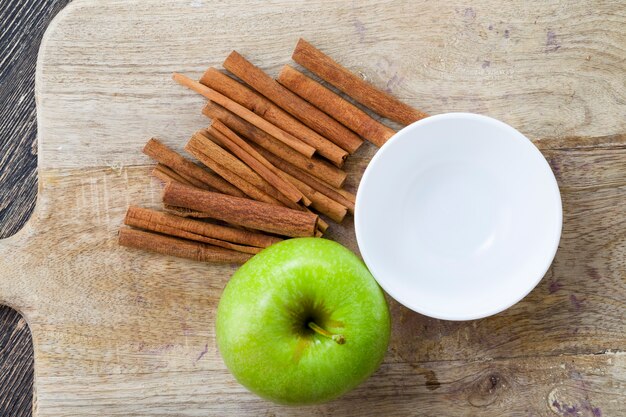 Reifer saftiger grüner apfel und duftender zimt auf einem hölzernen schneidebrett, nahaufnahme von lebensmitteln der natürlichen produktion, die in bio-bauernhöfen angebaut werden