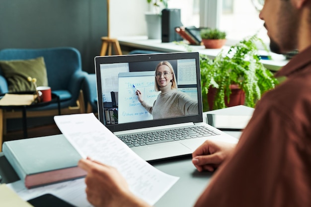 Reifer selbstbewusster Lehrer auf Laptop-Bildschirm, der auf Whiteboard zeigt