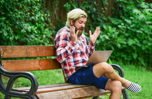 Reifer Student, der am Computer arbeitet, geht am Cyber-Montag einkaufen. Mann sitzt auf Bank mit Laptop, Online-Fernbildung, Hipster, inspiriert, im Park zu arbeiten. Agiles Geschäft