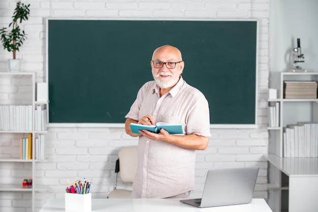 Reifes Lehrerporträt des Mannes des intelligenten Oberlehrers in den Gläsern mit Buch auf der Tafel im Unterricht an