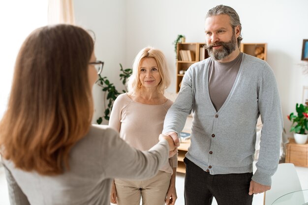 Reifes, ungezwungenes Paar, das seinen Immobilienberater im Büro begrüßt, während es nach einer neuen Wohnung oder einem neuen Haus sucht