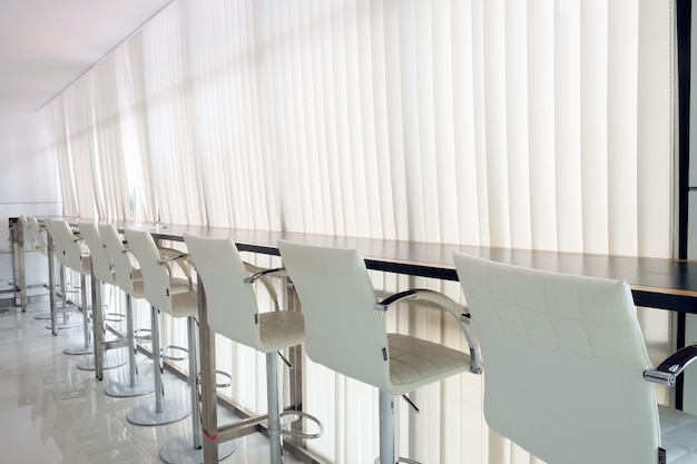 Reihe von Bar- oder Bürostühlen mit weißer Vorhangschiene und Sonnenlicht