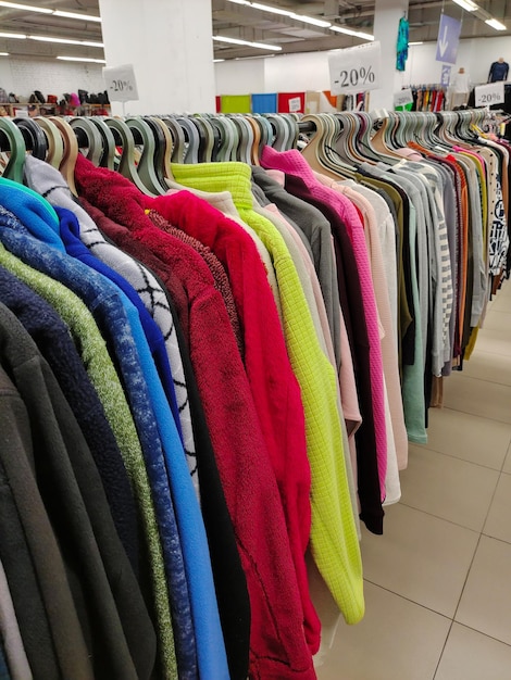 Reihen von Kleiderbügeln mit einer Vielzahl von bunten Roben und Hemden in einem Bekleidungsgeschäft in der Perspektive