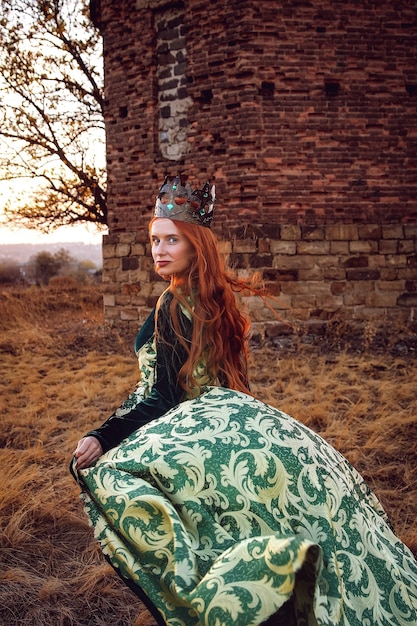 Reina con cabello rojo con un vestido verde con una corona y una espada