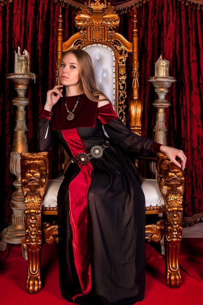 Reina medieval en traje histórico en el trono dorado en el castillo.  retrato de mujer joven con un vestido de estilo antiguo en un trono antiguo  en la sala de recepción de