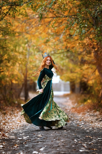 Reina con el pelo rojo con un vestido verde con una corona en el bosque