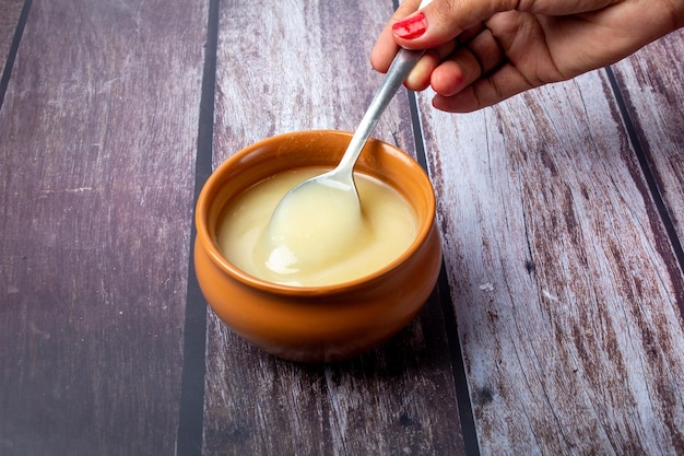 Reines Kuh-Ghee in Keramikschale auf Holzhintergrund mit Ghee-Löffel in der Hand