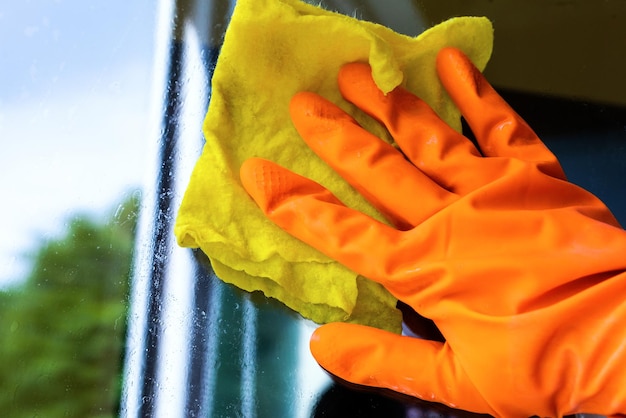 Reiniger in einem Handschuh wäscht ein Fenster orange-gelbes Tuch in der Nähe