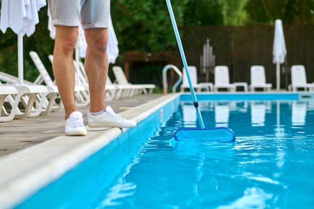 Reinigung des Beckens. Ein Servicemitarbeiter, der das Schwimmbad putzt und beschäftigt aussieht