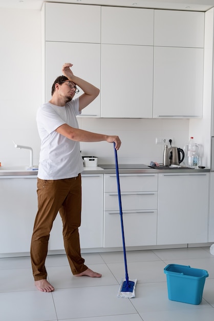 Reinigung und Desinfektion. junger Mann im weißen Hemd, der Küche mit Besen putzt