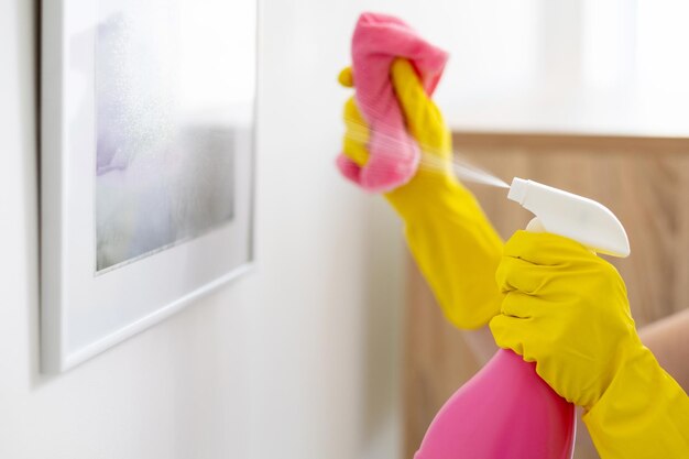 Reinigungsfirma Hausmeisterservice Professionelle Werkzeuge Hausarbeit Unerkennbare Frauenhände in gelben Schutzhandschuhen sprühen Bild mit Reiniger