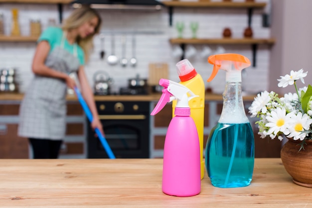 Foto reinigungsmittel und sprühflaschen auf hölzernem schreibtisch vor der frau, die zu hause wischt