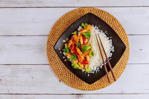 Reis mit gebratenem Huhn und Gemüse auf schwarzem quadratischem Teller. Chinesische Küche.