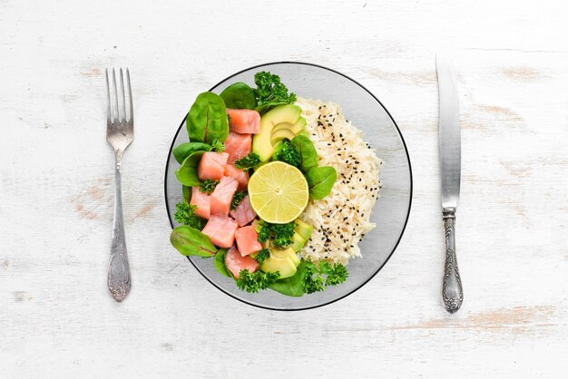 Reis mit Lachs, Avocado und Spinat In einer schwarzen Platte auf einem hölzernen Hintergrund Ansicht von oben Freier Platz für Ihren Text Flach lag