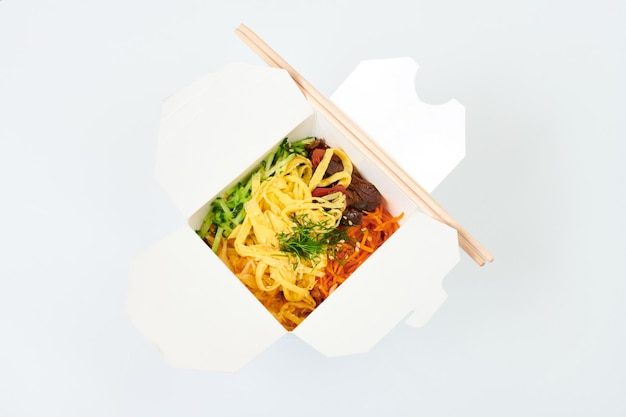 Reis-Wok mit Meeresfrüchte-Cocktail und Gemüse in Box und Holzstäbchen isoliert auf weißem Hintergrund, Studio. Offene Take-Away-Box mit Wok und Bambusstäbchen. Fast-Food-Konzept zum Mitnehmen und Mitnehmen