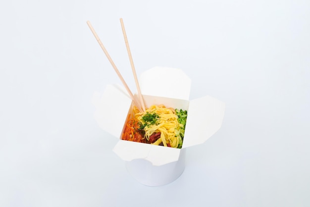 Reis-Wok mit Meeresfrüchten und Gemüse in weißer Kiste und Holzstäbchen isoliert auf weißem Hintergrund, Nahaufnahme. Offene Take-Away-Box mit Wok und Bambusstäbchen. Asiatisches Essen, Fast-Food-Lieferkonzept