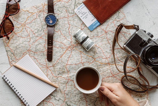 Reise-Flat-Lay-Konzept mit Reiseartikeln in der Hand mit einer Tasse Kaffee über einer Vintage-Karte