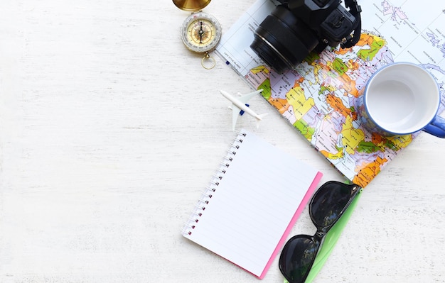 Reise-Hintergrund-Konzept Planung Wesentliche Urlaubsreiserzeugnisse Sommerreiserzüge mit Kamera Sonnenbrille Kompasskarte Notebook Kaffeetasse und Flugzeug für Reisende auf weißem Holz